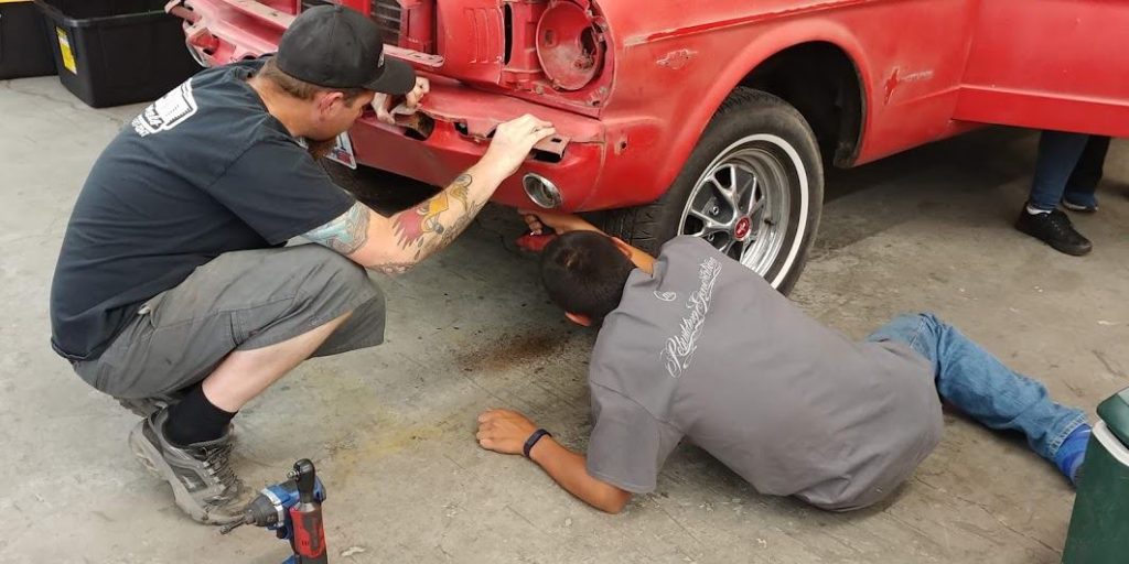 A mentor and a youth inspecting a bumper