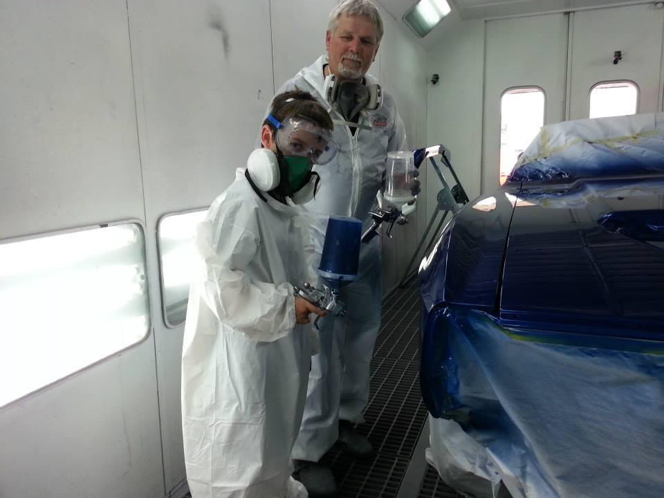 A young kid with his mentor in the paint booth